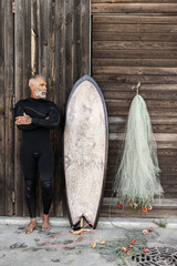 Vertical shot of a mature male in a wetsuit with a surfing board - obrazy, fototapety, plakaty