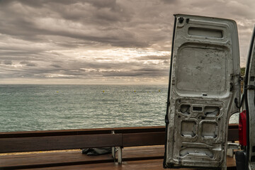 Close-up shot of an opened van door with a background of ocean and cloudy sky.