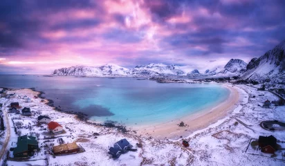 Fototapeten Luftaufnahme des nordischen Sandstrandes, Meer im Winter bei Sonnenuntergang. Lofoten-Inseln, Norwegen. Landschaft mit schneebedeckten Bergen, violettem Himmel mit Wolken, azurblauem Wasser, Häuser in der Abenddämmerung. Natur. Ansicht von oben. Kalter Ab © den-belitsky