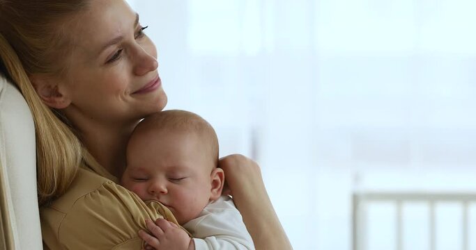 Happy serene mother sit in armchair cuddle caress tender baby napping on her shoulder look at distance dream of good health happy future for kid. Smiling relaxed mom guard sweet sleep of infant child