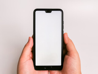 Hand holds black smartphone with blank screen against white background.