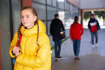 Portrait of female teenage student with braids in warm yellow puffer jacket on her way to college...