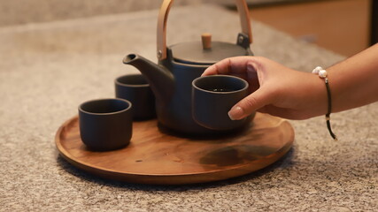 Una joven coge una tetera para servir el té, bandeja de estilo japonés