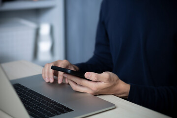 Male using smartphone and laptop online working home workspace urban life