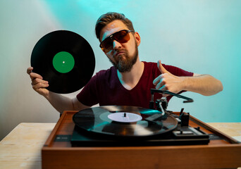Man with vinyl in his hand in front of turntable showing thumbs up, wearing disco 80s sunglasses 