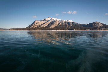 Mount Michener in late afternoon light reflects down onto the frozen surface of Abraham Lake in the...