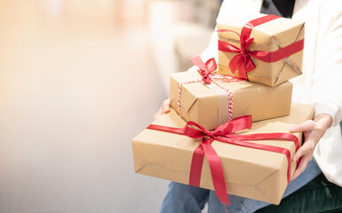 Female hands holding Christmas gift box with red bow and brown paper wrap for Xmas and New Year celebrate party