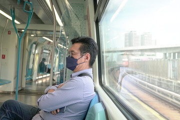 Asian man commuter with face mask on inside a moving subway train. Masked transit concept.