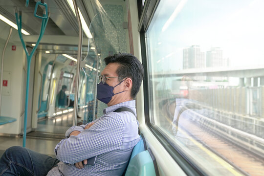 Asian Man Commuter With Face Mask On Inside A Moving Subway Train. Masked Transit Concept.