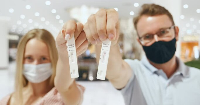 Couple man and woman show their negative COVID-19 antigen test results to the camera. Coronavirus pandemic precautions. People with self-test for covid wearing face mask