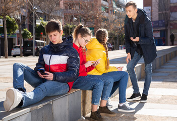 Obraz na płótnie Canvas Four teenagers chatting on their smartphone on walking