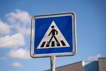 Pedestrian crossing traffic sign in Germany. Person walking on zebra stripes on a blue square road sign. Rules for car drivers on the street. Warning to call attention to people crossing the way.