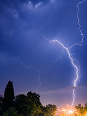 Bright lightning sparkles with a beautiful pattern in the evening sky over the city and trees