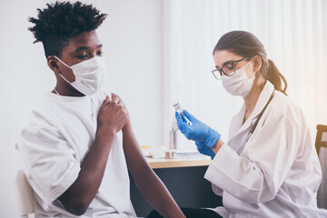 Doctor giving vaccine to african boy wearing face mask during coronavirus or covid-19 pandemic at hospital,Vaccination concept