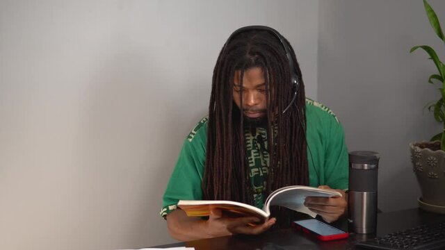African American Man reading a book at desk wearing headset