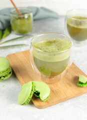 Matcha tea in a glass and green macaroon cake on a wooden bamboo tray. Close-up on a gray background.