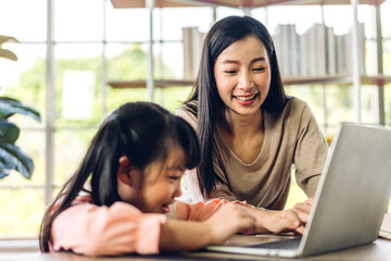 Mother and asian kid little girl learn and look at laptop computer reviewing lesson study with...