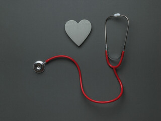 A red stethoscope and a gray wooden heart on a dark gray background. The concept of medical...
