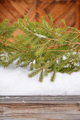 Winter decoration of fir branches on a snowdrift on a blurred wooden background. Vertical frame, copy space