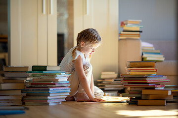 A little cute girl in a yellow dress reading a book sitting on the floor