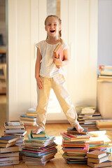 cute little girl is reading book and standing on pile of books. Children and education