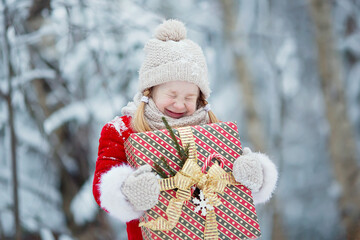 Little funny child dressed in Santa Claus red costume bringing presents in winter snowy forest. Christmas Eve 