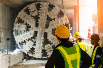 Engineer wear yellow helmets,vests safety are discussing.Technician control underground tunnel construction at working shaft.Transport pipeline by Tunnel Boring Machine(TBM) method for electric train - obrazy, fototapety, plakaty