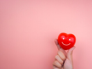 The smiling face on red heart ball in people hand on pink pastel background with copy space....