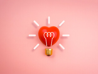 Fototapeta premium Light bulb icon on red heart ball on pink pastel background, minimal style. Love, care, sharing, giving, wellbeing, inspiration, and idea concepts.