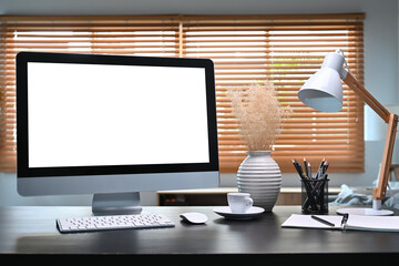 Front view computer with empty screen, supplies and lamp on black table.