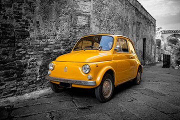 Yellow vintage car isolated on grayscale town background Tuscany, Italy