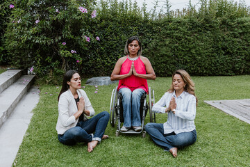 Latin business woman transgender on wheels chair and friends sitting on grass and meditating at...