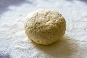 Fresh raw dough on a dark background, sprinkled with flour.