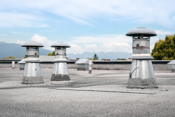 Flat roof vents on building with 2-ply SBS or modified bitumen roofing system. Group of metal ventilators such as: bathrooms and laundry exhaust and plumbing stack vent. Selective focus. - Powered by Adobe