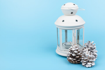 White lantern with candle inside and Christmas decoration on blue background. Copy space.