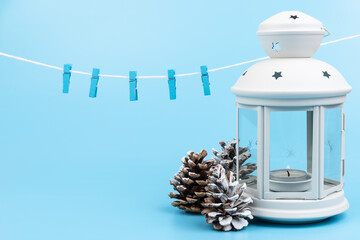 White lantern with candle inside and Christmas decoration on blue background. Copy space.