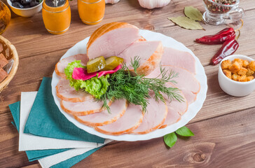 Sliced ham on a white plate on a wooden background.