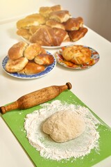 Raw dough and wooden rolling pin near delicious fresh homemade sweet and meat pies on white table in kitchen close view