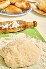 Raw dough and wooden rolling pin near delicious fresh homemade sweet and meat pies on white table in kitchen extreme close view