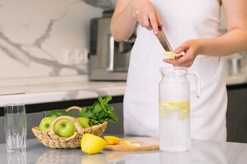 Woman making detox drink with lemon and mint in the kitchen at home. Rejuvenating invigorating water lemon, antioxidant.