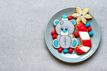 gingerbread cookies decorated with glaze in shape of bear in hat, lollipop, snowflakes on plate on gray background Top view Flat lay Christmas treats, sweets concept New year party Holiday card