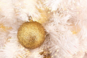 Fir branch with ball and festive lights on the Christmas background with golden sparkles.