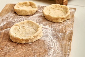 Pies forms of raw dough prepared for adding different fillers on rustic wooden boards on white...