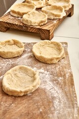 Fototapeta na wymiar Pies forms of raw dough prepared for adding different fillers on rustic wooden boards on white table in kitchen close view
