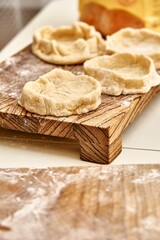 Pies forms of raw dough prepared for adding different fillers on rustic wooden boards on white table in kitchen close view