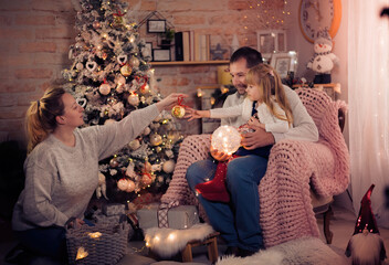 Merry Christmas and Happy Holidays! Dad, Mom and daughter decorate the Christmas tree indoors. The morning before Xmas. Portrait loving family close up. - 475972440