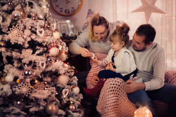 Merry Christmas and Happy Holidays! Dad, Mom and daughter decorate the Christmas tree indoors. The morning before Xmas. Portrait loving family close up. - 475972445