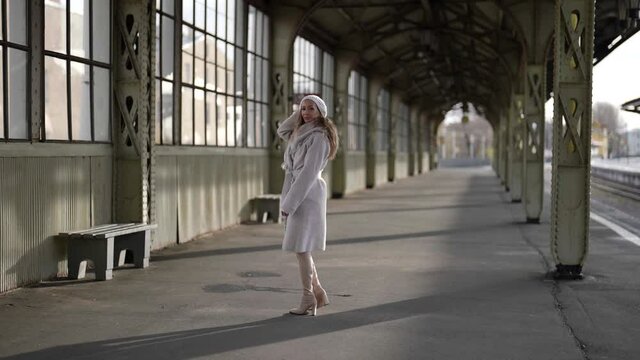 winter walk in old railway station, woman in white coat and beret is strolling and sitting on bench