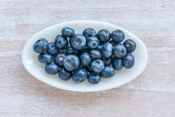 Blueberries on an oval plate on a wooden table. View from above.