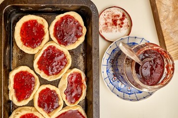 Raw open pies filled with delicious homemade currant jam in large baking dish on white table in kitchen upper close view